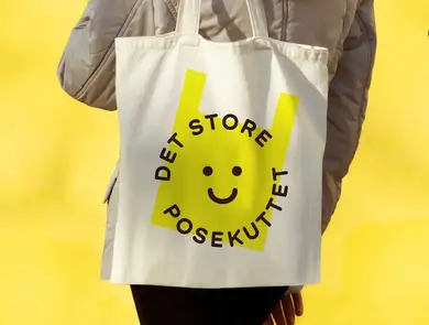 En person i beige jakke bærer på et lyst nett med en tegnet gul pose på. gul bakgrunn på bildet