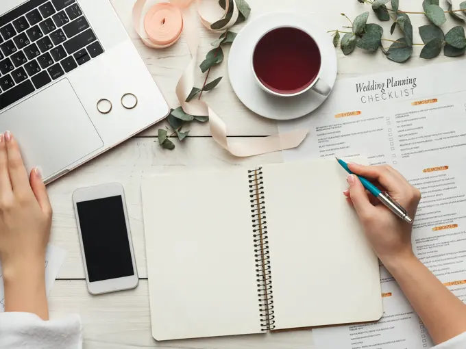Wedding arrangement background. Female hands preparing for marriage, using laptop, smartphone, paper calendars and planners, top view. Bridal wallpaper with copy space on to do list