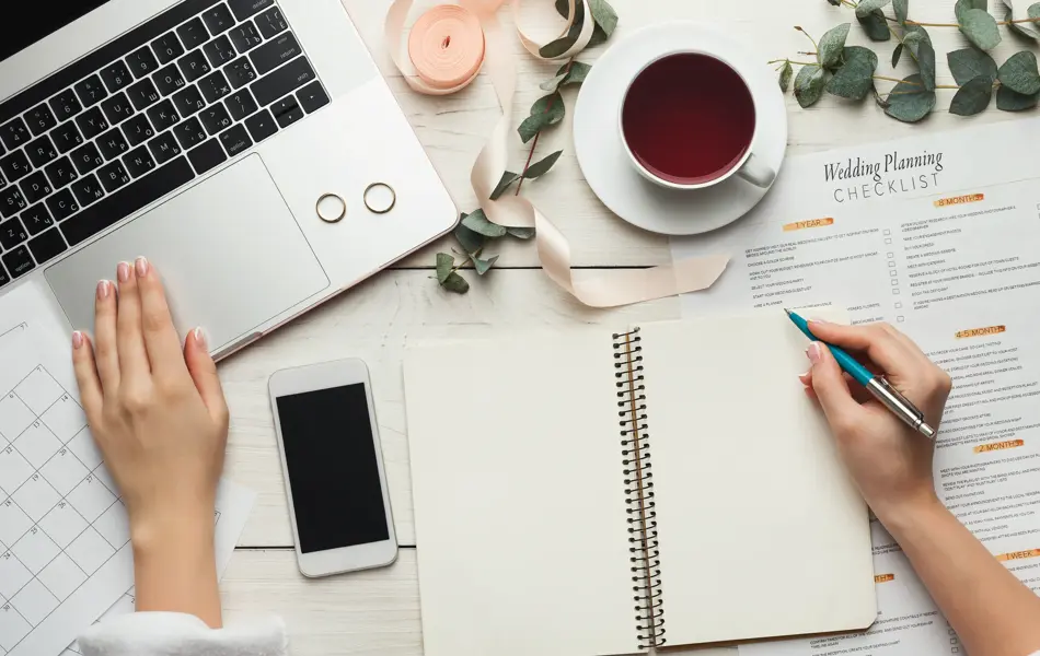 Wedding arrangement background. Female hands preparing for marriage, using laptop, smartphone, paper calendars and planners, top view. Bridal wallpaper with copy space on to do list