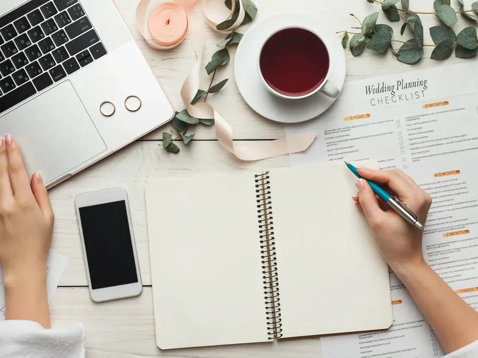 Wedding arrangement background. Female hands preparing for marriage, using laptop, smartphone, paper calendars and planners, top view. Bridal wallpaper with copy space on to do list