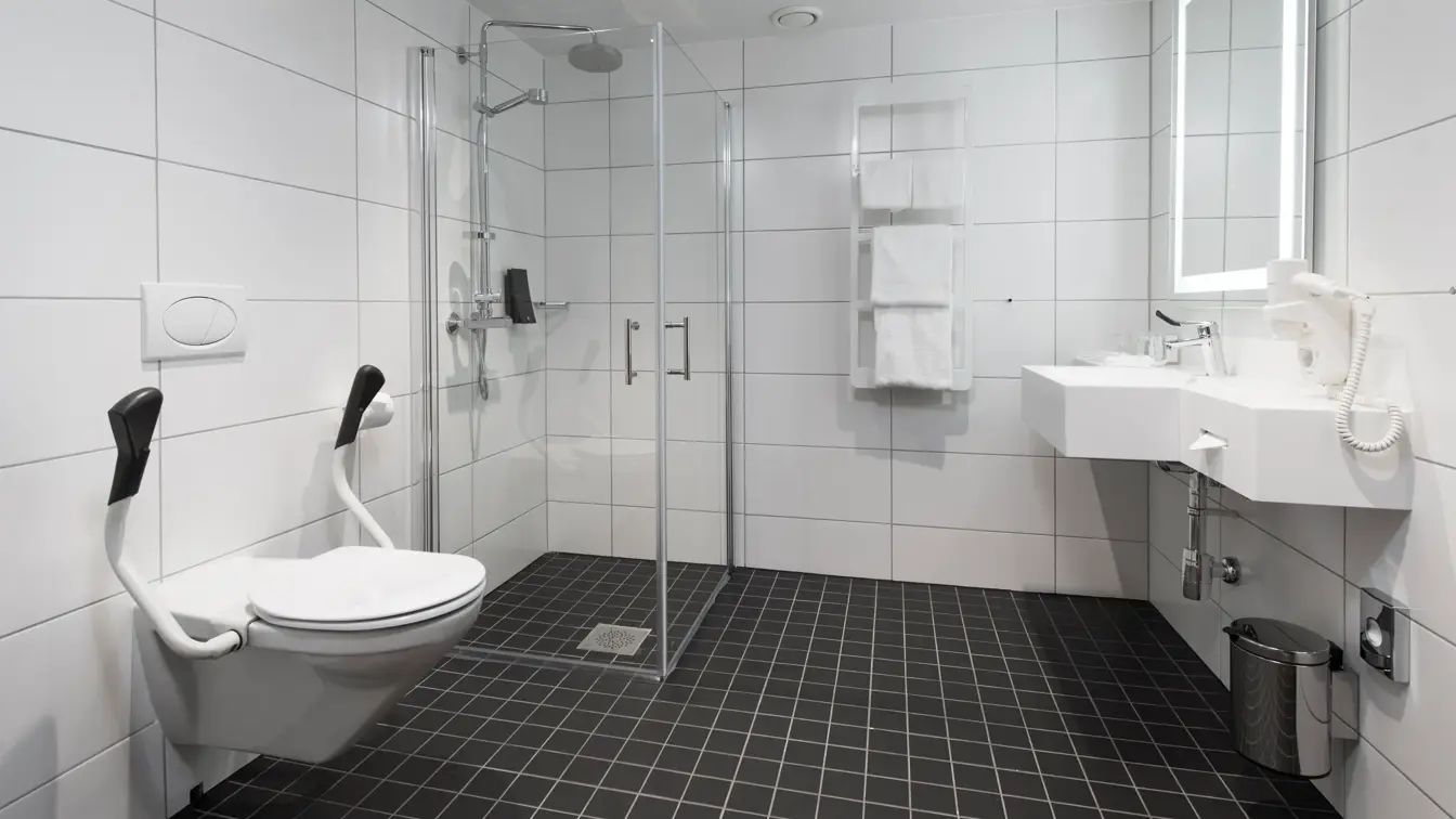 Toalett med støttearmer, mye gulvplass, dusj, vask og speil på bad i handikaprom på Thon Hotel Rosenkrantz Oslo, som ligger i Oslo sentrum