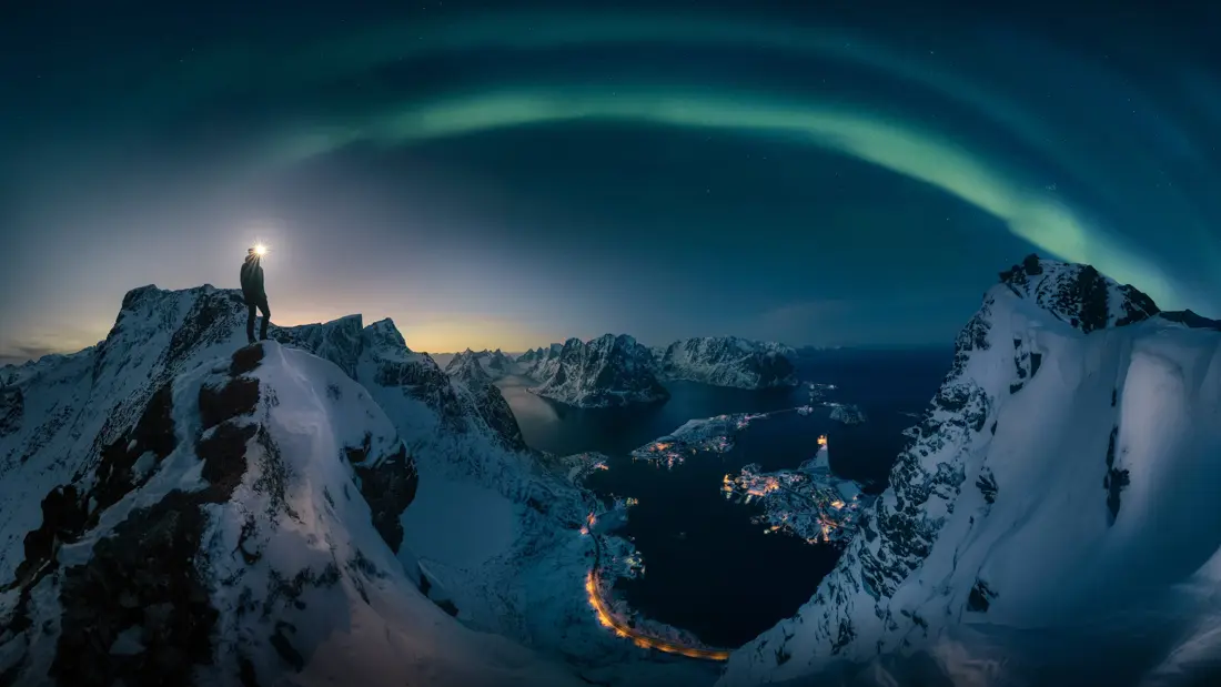 A man hiking on Reinebrigen, mountain in Lofoten Norway , Northern light over the mountain