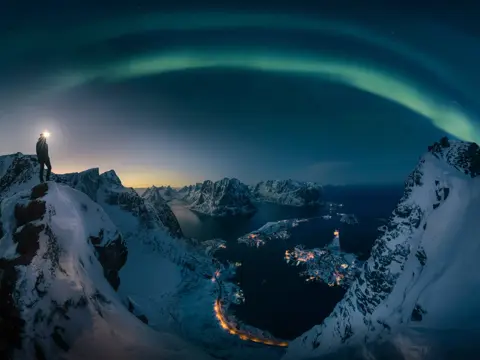 A man hiking on Reinebrigen, mountain in Lofoten Norway , Northern light over the mountain