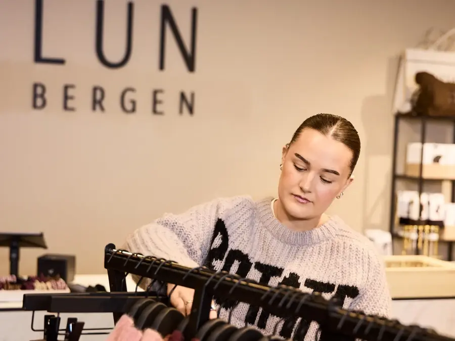 jente som rydder stativ i motebutikk åsane