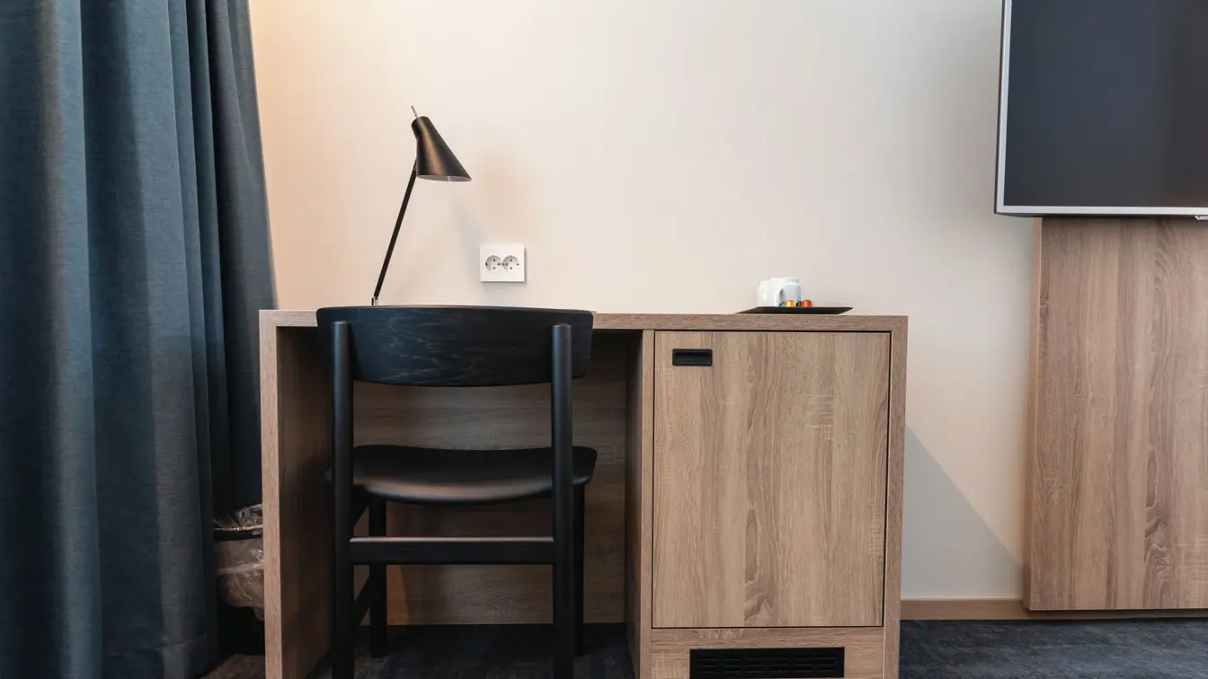 Skrivebord i lyst træ, sort stol og leselampe. Mørkegrå gulvteppe og vegghent TV. I superior room på Thon Hotel Norge i Kristiansand.