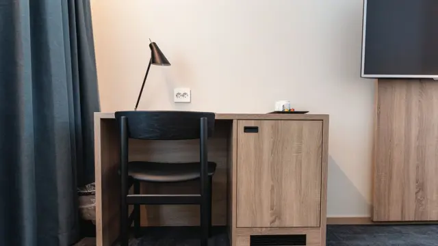Skrivebord i lyst træ, sort stol og leselampe. Mørkegrå gulvteppe og vegghent TV. I superior room på Thon Hotel Norge i Kristiansand.