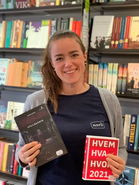 smilende norli-ansatt med brunt hår som holder frem to bøker