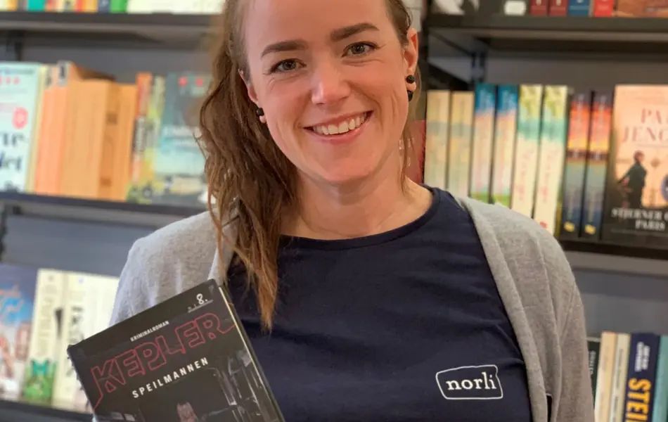 smilende norli-ansatt med brunt hår som holder frem to bøker