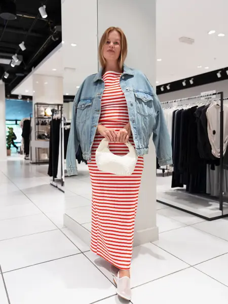 Damemodell med rød og hvit stripet lang kjole, hvit veske og olajakke