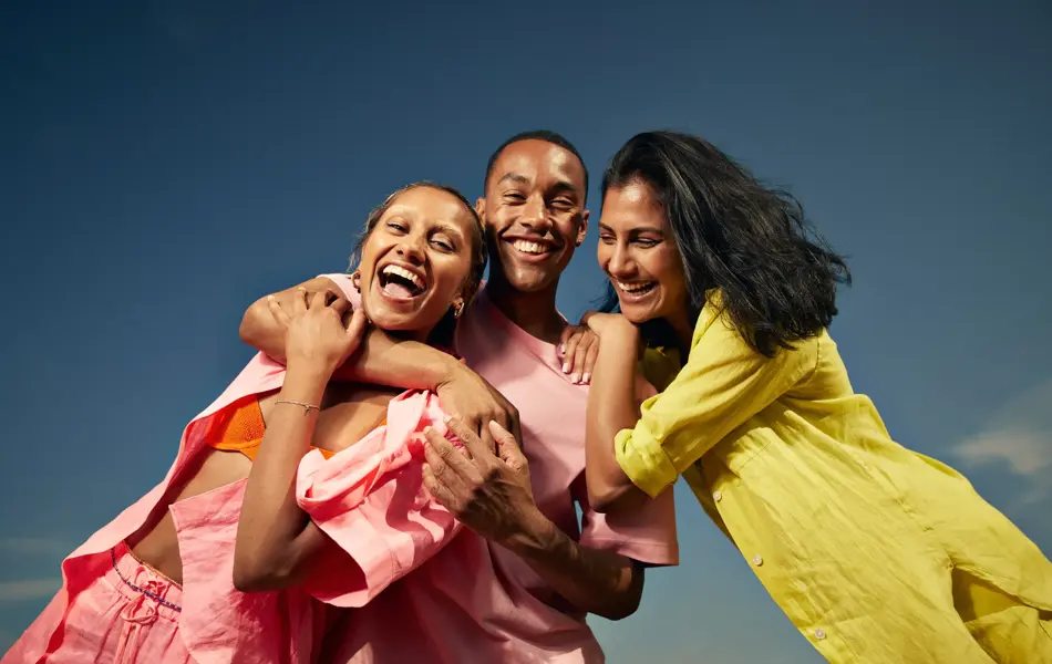 Tre venner med rosa og gule antrekk smiler mot kamera 