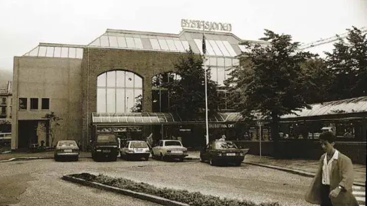 Svart-hvitt bilde av en bygning med bilder og folk foran