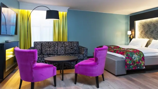 Dobbeltseng med mønstrede sengeteppe og lilla stol, zebramønstret sofa og to lilla stoler i sittegruppe, TV og gule gardiner på buisness room på Thon hotel Terminus i Oslo sentrum nær Jernbanetorget