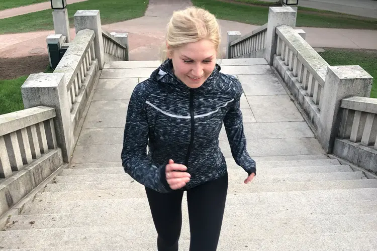 Dame i treningstøy som jogger opp en trapp ute.