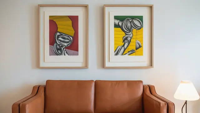 Lysebrun skinnsofa, hvite vegger og to store fargerike bilder. I suite på Thon Hotel Norge i Kristiansand.