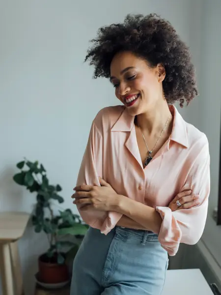 Smilende dame med lys ferskenfarget skjorte og lys jeans står med armer i kors