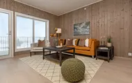 Bilde fra visningsleiligheten i Høyfjellstunet på Skeikampen. Bildet viser stuen med oransje sofa, trepanel på veggene og fint lys fra vinduene.