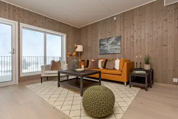 Bilde fra visningsleiligheten i Høyfjellstunet på Skeikampen. Bildet viser stuen med oransje sofa, trepanel på veggene og fint lys fra vinduene.