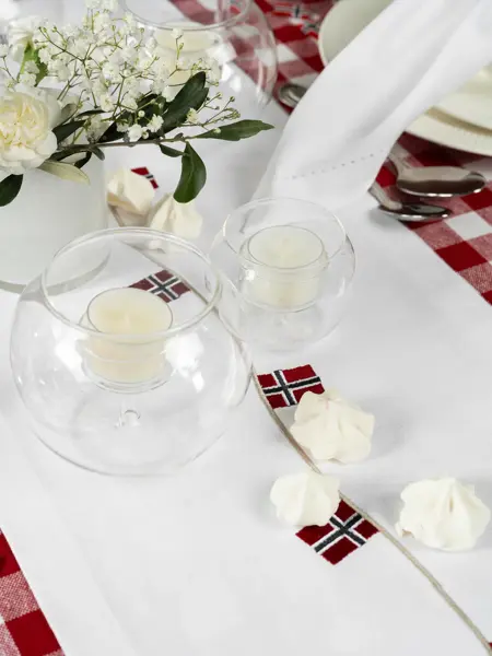 Bord dekket med hvit løper, telysholdere, hvite pikekyss, liten vase med hvite blomster.