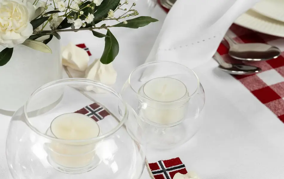 Bord dekket med hvit løper, telysholdere, hvite pikekyss, liten vase med hvite blomster.