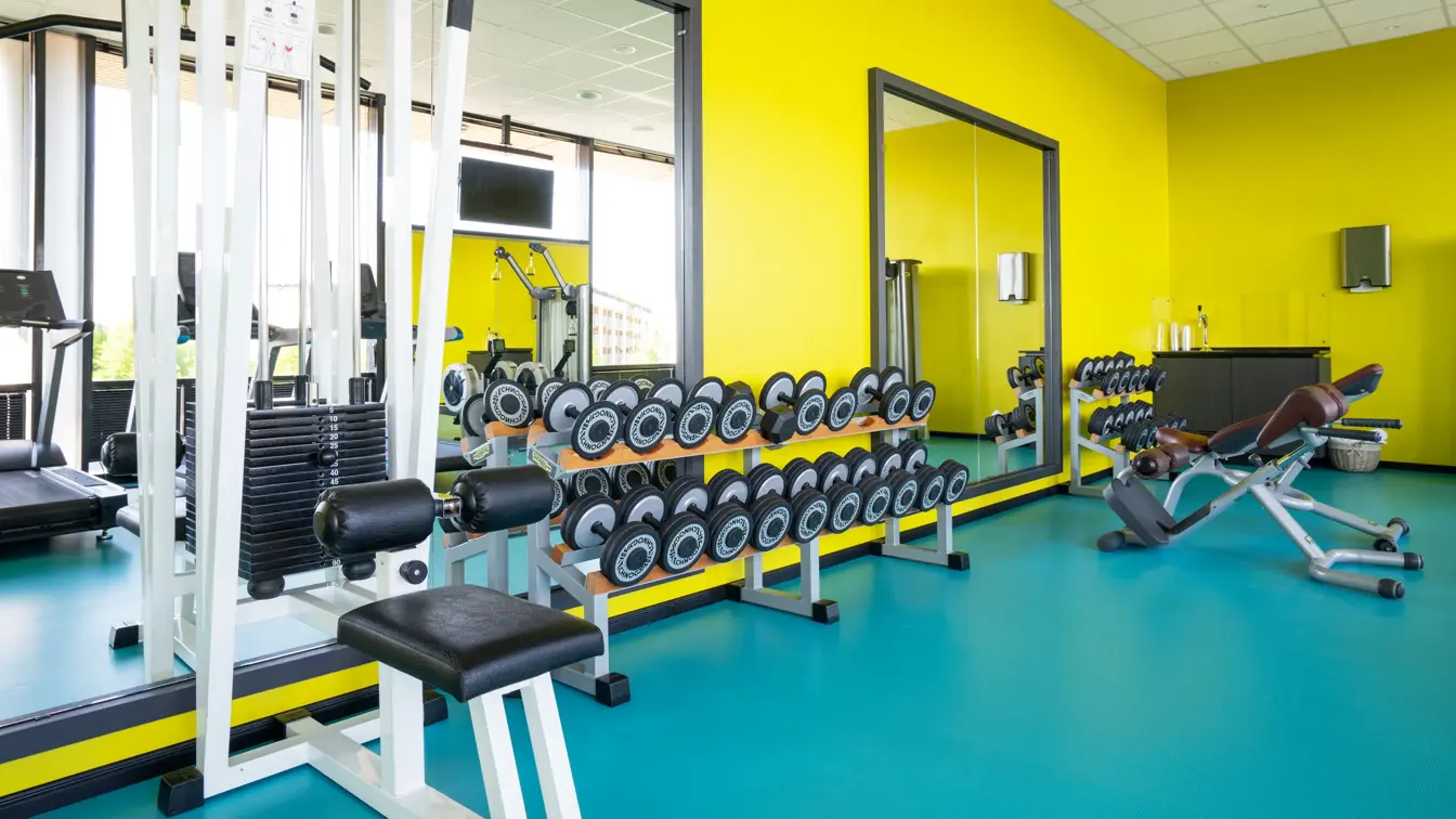Styrkeapparat og manualer foran speil med gule vegger og turkisk gulv på treningsrom på Thon Hotel Arena i Lillestrøm