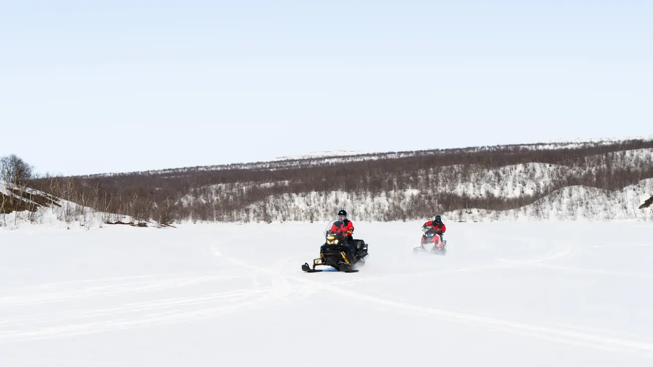 To person kjører snøscooter etter hverandre sett fra avstand i snødekt landskap