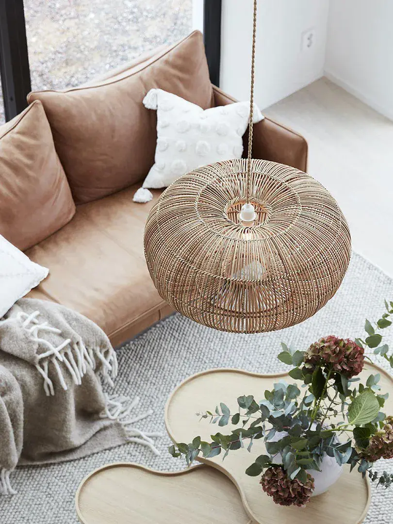 Rotting taklampe henger over en skinnsofa og to avlastningsbord med en vase med blomster i.