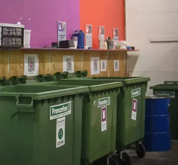 Godt organisert avfallsrom med grønne avfallsdunker og fargekoder og gjenstander på veggen som forklarer hva som kan kastes i disse avfallsdunkene.