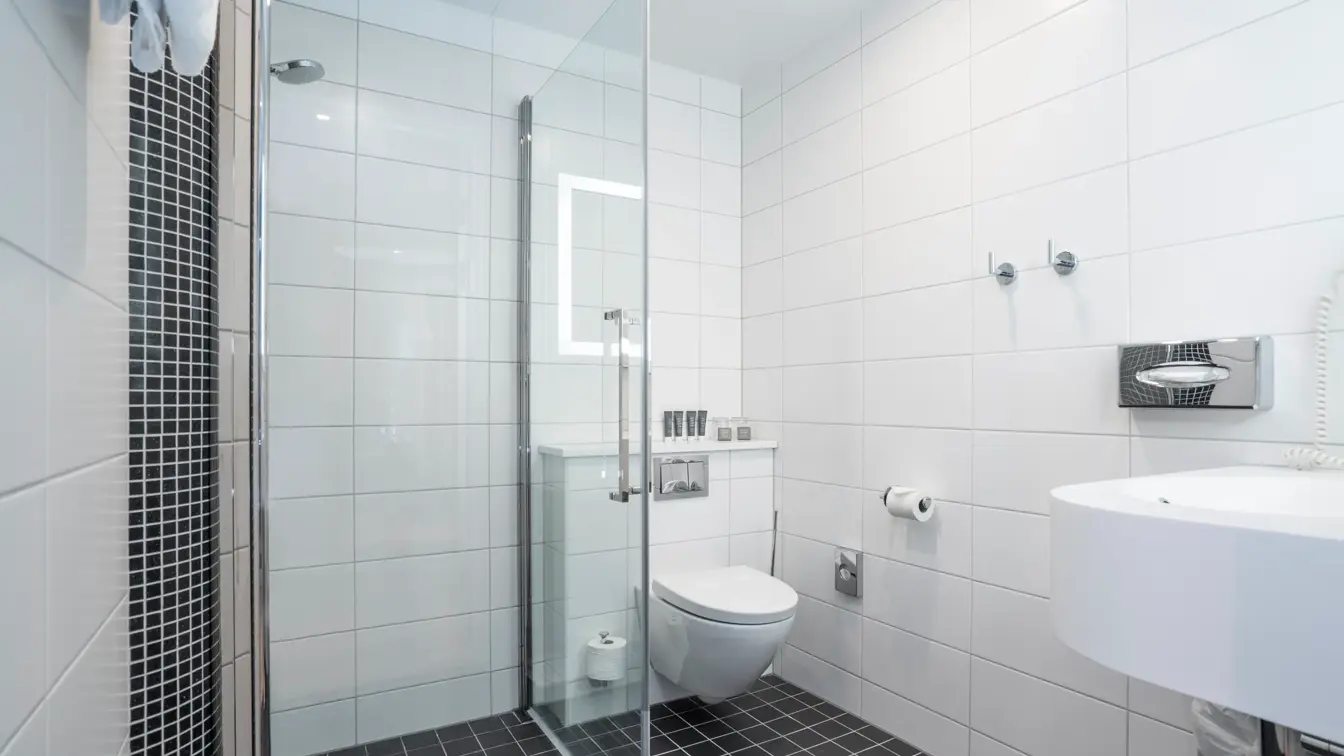 Svarte gulvfliser, hvite veggfliser, dusj, toalett, vask.