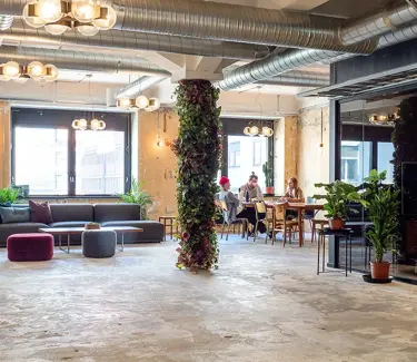 Interiør fra kontoret til The Oslo Company, stor og åpen sosial sone med rustikke detaljer som betonggulv og ventilasjon, grønne planter og lyse farger på veggene