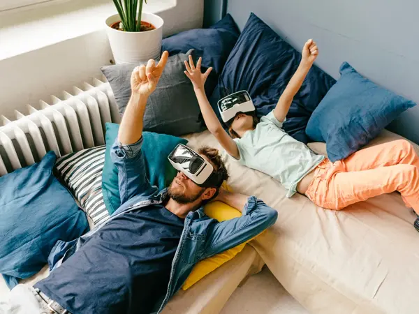Fugleperspektiv på mann og jente som ligger i senga med VR-briller. Foto til artikkel om gaver til pappatyper på farsdag.