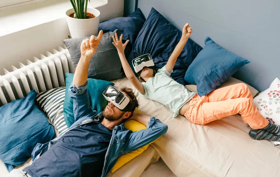 Fugleperspektiv på mann og jente som ligger i senga med VR-briller. Foto til artikkel om gaver til pappatyper på farsdag.