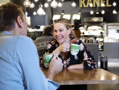 to personer med skravlekopper sitter og prater på kafè