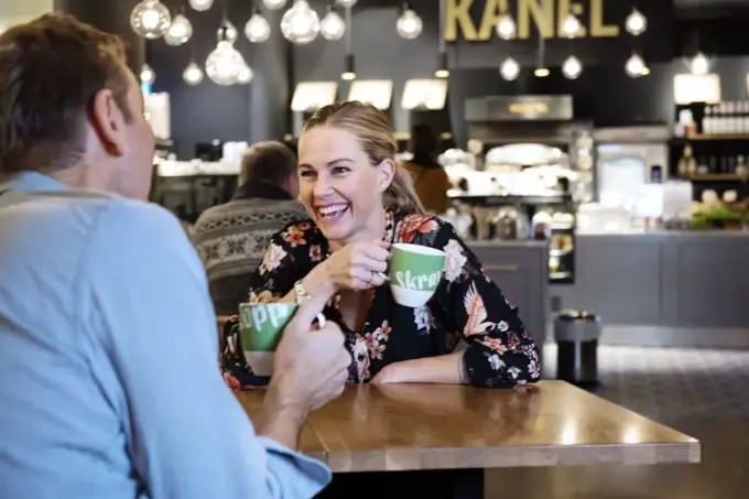 to personer med skravlekopper sitter og prater på kafè