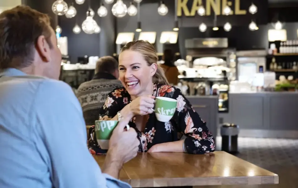 to personer med skravlekopper sitter og prater på kafè