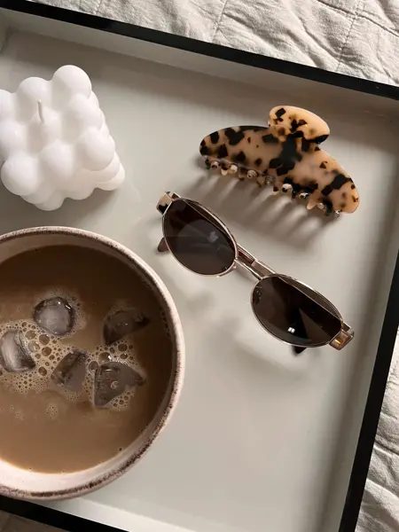 Solbriller, hårklype, kopp med iskaffe og et kubelys på et fat