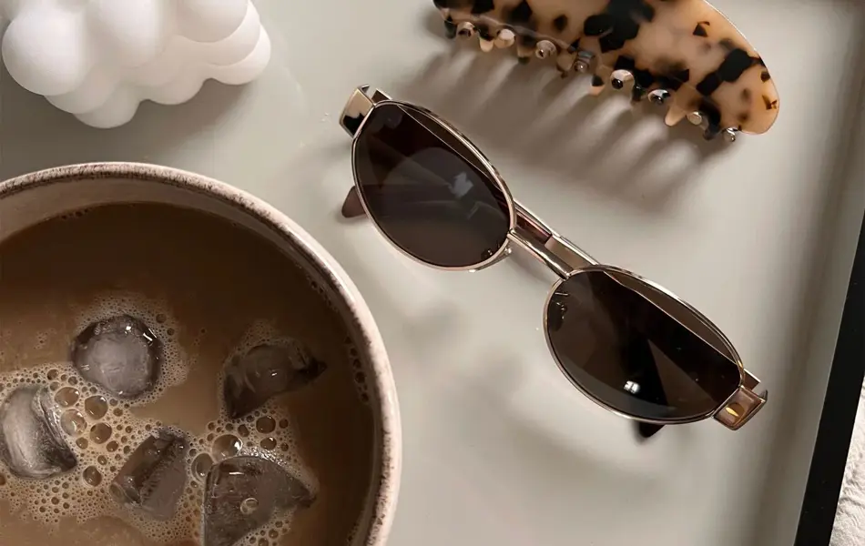 Solbriller, hårklype, kopp med iskaffe og et kubelys på et fat