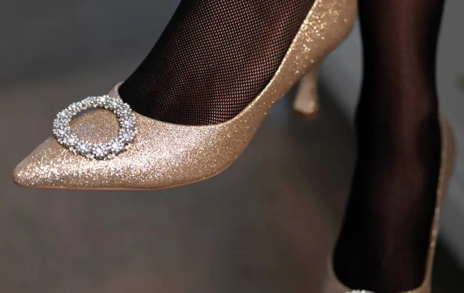 Ben med sort strømpebukse og gullglitrende pumps med pyntestener foran.