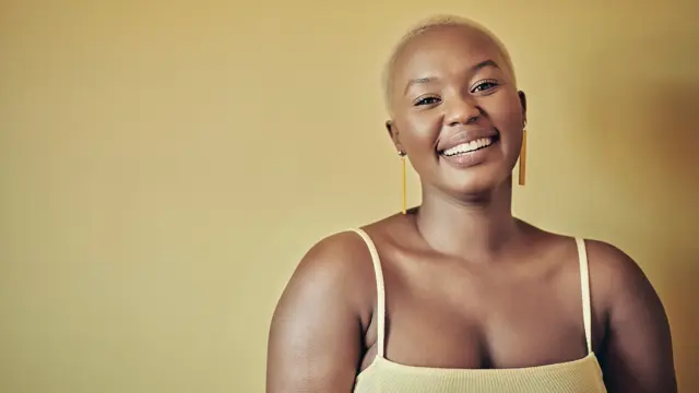 Smilende dame med lys gul singlett står mot gul bakgrunn 