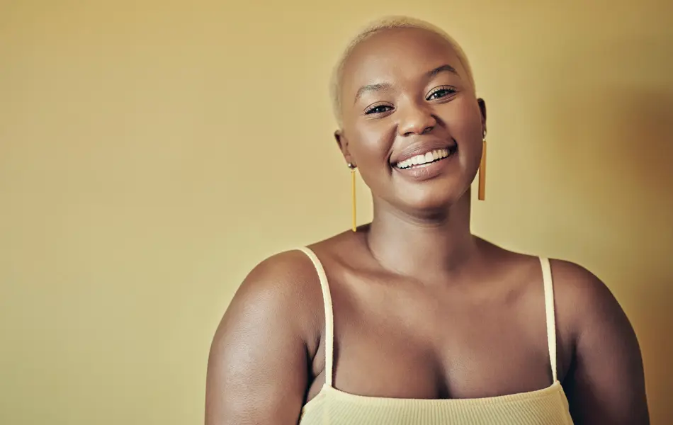 Smilende dame med lys gul singlett står mot gul bakgrunn 