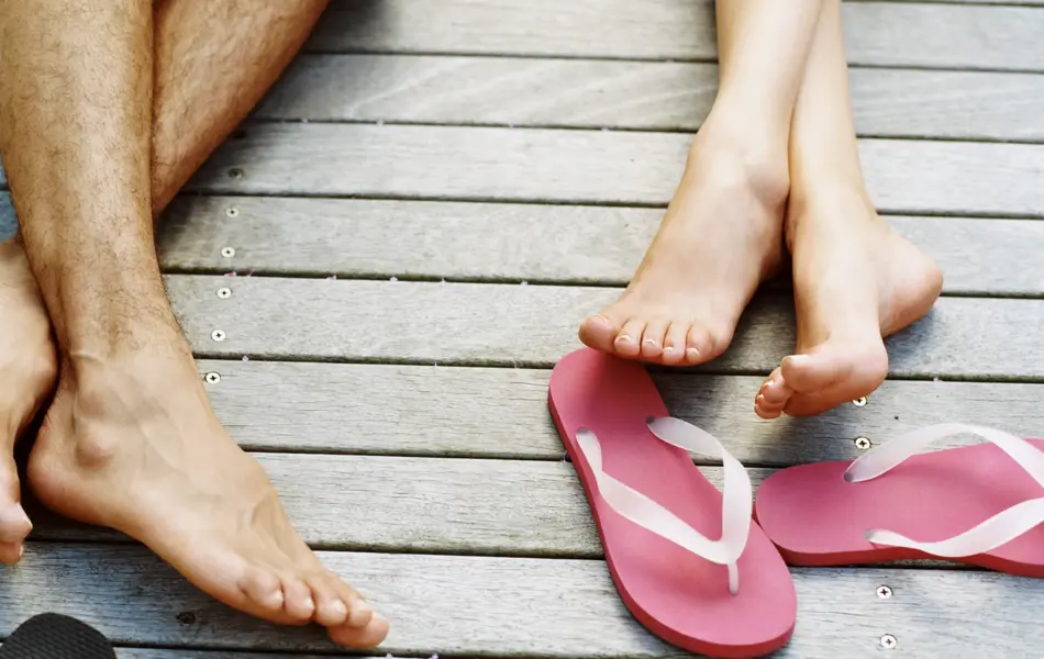 Nærbilde av to par ben på brygge med flip flops 