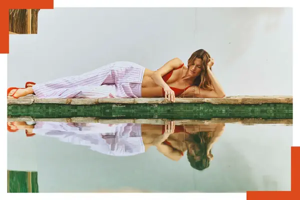 Dame ligger ved bassenget i stripete bukse, rød bikinitopp og flip flops. 