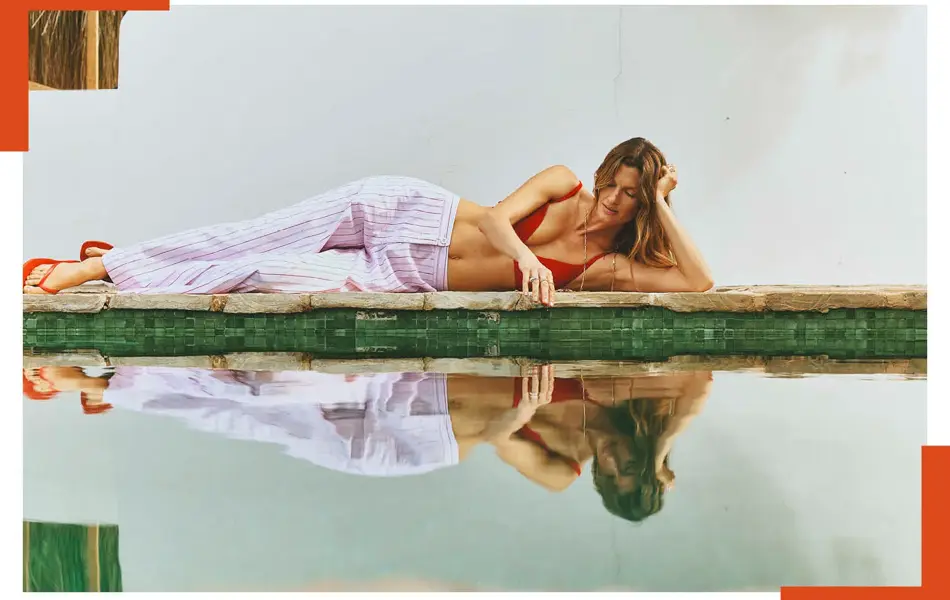 Dame ligger ved bassenget i stripete bukse, rød bikinitopp og flip flops. 