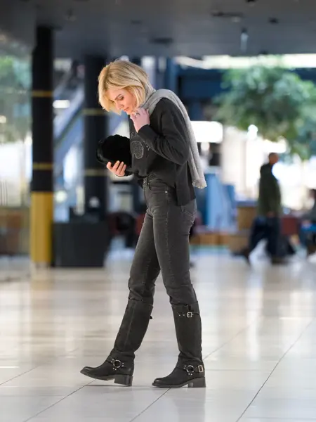 Dame i sort genser, grått skjerf, sorte jeans og sorte høye boots.