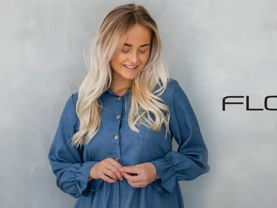 Dame med lyst hår og blå kjole, logo til Floyd på veggen bak henne