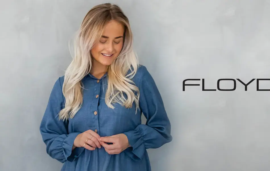 Dame med lyst hår og blå kjole, logo til Floyd på veggen bak henne