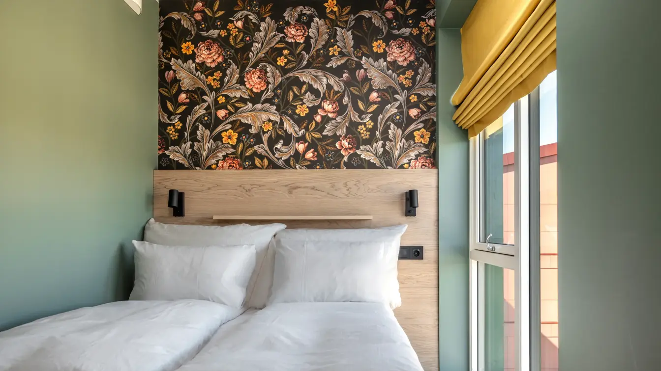 Standard queen rom med queen seng, hvitt sengetøy, mønstrete tapet bak sengen, grønne vegger, stort vindu og gul gardin.