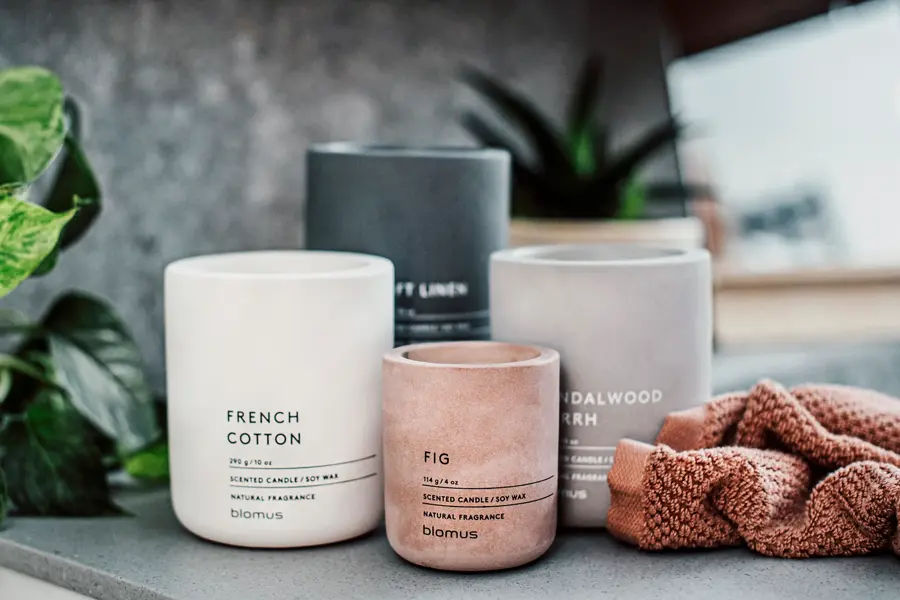 Fire krukker med duftlys, en grønn plante og en rustfarget klut 