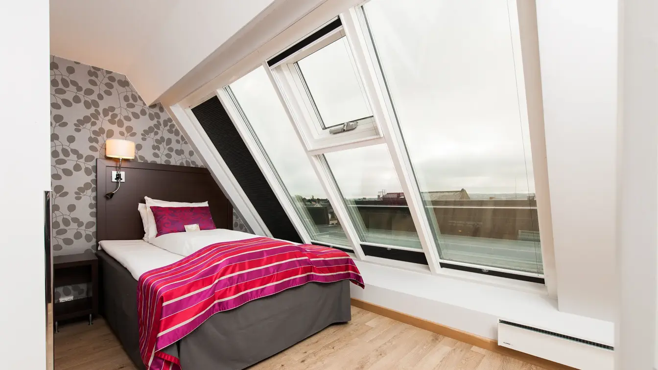 Skråtakvinduer, enkeltseng, nattbord, tapetvegg. 