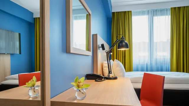 Speil. skrivebord med rød stol, blå vegger, dobbeltseng og gule gardiner i dobbeltrom på Thon Hotel Astoria