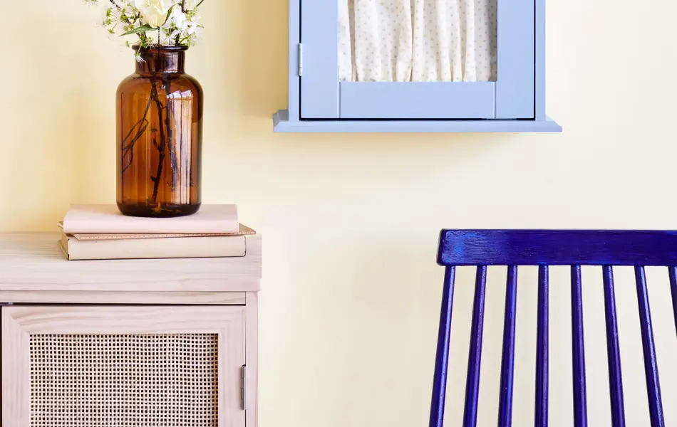 Gul vegg med blått skap, kommode og blomstervase